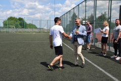 Dyrektor szkoły wręcza puchar uczniowi, w tle inne osoby, siatka