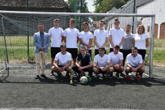 Dyrektor, nauczyciele i uczniowie pozują do zdjęcia w bramce, przed nimi stoi puchar, obok piłka