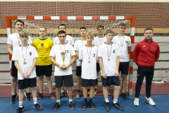 Nauczyciel i uczniowie z medalami na szyi pozują do zdjęcia na stojąco