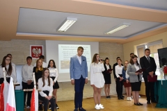 Uczniowie w strojach galowych stoją, w tle godło i flaga polski