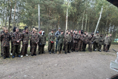 Grupa osób w strojach moro stoi, w tle drzewa
