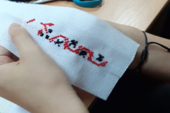 W rękach trzymany jest kawałek białego materiału z czerwono-czarnym haftem