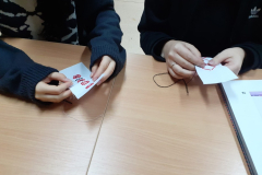 W rękach trzymany są kawałki białego materiału z czerwono-czarnym haftem