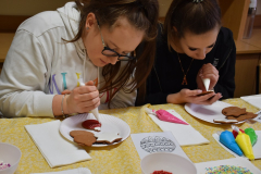 Uczennice w rękach trzymają woerczki z lukrem, przed nimi na stole leżą pierniki, lukier i serwetki