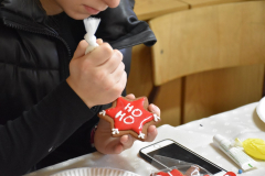 W jednej ręce trzymany jest lukier w woreczku w drugiej lukrowany piernik z napisem HO HO