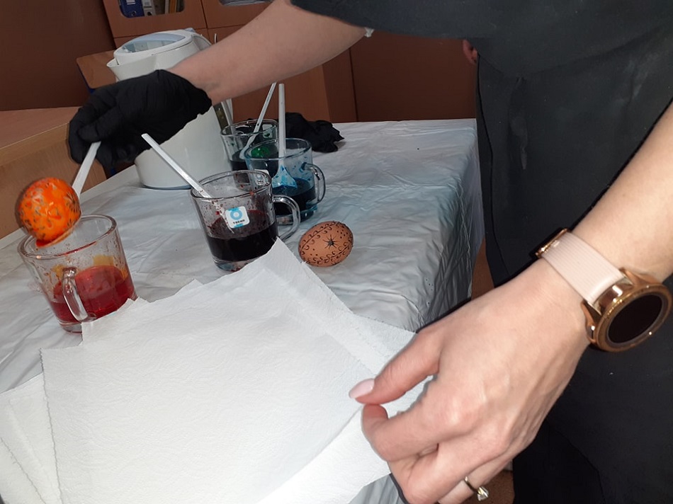 Zdjęcie przedstawia barwnik w szklance stoi na ławce, obok leży ubarwiona pisanka woskowa