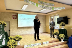 Starosta Powiatu Piotrkowskiego stoi z mikrofonem w ręku, obok stoi dyrektor szkoły