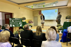 Kobieta i mężczyzna stoją na scenie, grupa osób siedzi