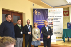 Kobieta i mężczyźni stoją, w tle banery z napisami Powiat Piotrkowski oraz Zespół Szkół Centrum Kształcenia Ustawicznego im. Juliusza Poniatowskiego w Czarnocinie,kształcimy w zawodach