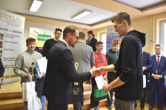 Mężczyzna wręcza uczniowi puchar i nagrodę, w tle inne osoby