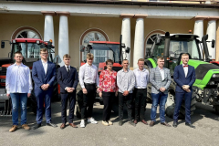 Uczniowie i nauczycielka pozują do zdjęcia, w tle traktory