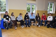 Uczniowie siedzą na krzesłach w tle okna