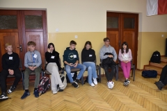 Uczniowie siedzą na krzesłach w tle drzwi