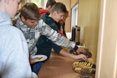Uczniowie stoją i nakładają na talerze ciasto