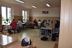 Uczniowie siedzą przy stołach w tle okna