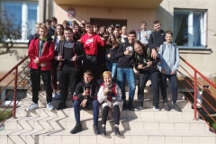 Uczniowie i nauczycielka siedzą na schodach, w tle okna, ściana