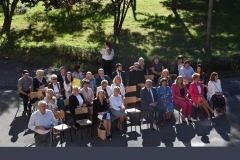 Nauczyciele siedzą, w tle drzew, trawa