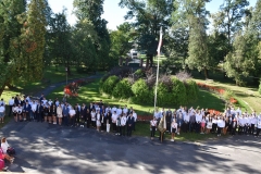 Uczniowie stoją, w tle drzew, flaga na maszcie