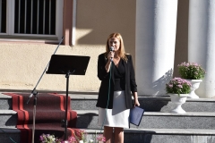 Zastępca Wójta Gminy Czarnocin stoi, w ręku trzyma mikrofon, w tle schody, kwiaty