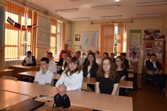 Uczniowie siedzą w ławkach, w tle okna