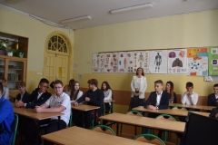 Uczniowie siedzą w ławkach, w tle ściana z planszami