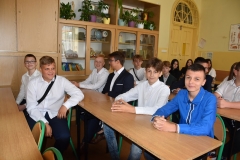 Uczniowie siedzą w ławkach, w tle szafy