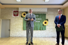 Jeden mężczyzna stoi przy mikrofonie, drugi stoi obok, w tle słoneczniki