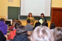 Uczniowie siedzą w ławkach, dwie kobiety stoją, w tle tablica