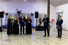 Wójt trzyma mikrofon w ręce, obok stoi dyrektor szkoły oraz uczniowie