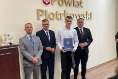 Mężczyźni na stojąco pozują do zdjęcia, nad nimi napis Powiat Piotrkowski
