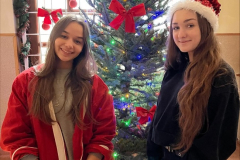 Uczennice w czapkach Mikołaja na głowie stoją obok choinki