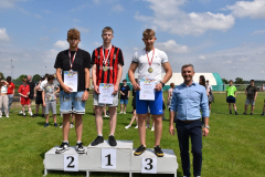 Chłopcy z medalami na szyi i dyplomami w ręku stoją na podium, obok stoi dyrektor szkoły