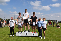 Chłopcy z medalami na szyi i dyplomami w ręku stoją na podium, obok stoją dyrektor szkoły i nauczyciele