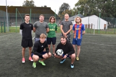 Czworo uczniów stoi na boisku, dwóch uczniów kuca w rękach trzymają piłki