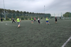 uczniowie biegną za piłką na boisku, w tle drzewa