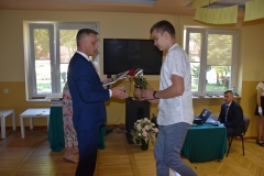 Dyrektor szkoły wręcza uczniowi nagrodę, w tle okno, telewizor