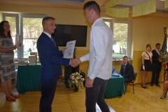 Dyrektor szkoły wręcza uczniowi nagrodę, w tle okno, telewizor