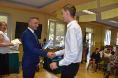 Dyrektor szkoły wręcza uczniowi nagrodę, w tle okno, telewizor