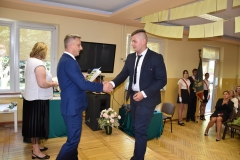 Dyrektor szkoły wręcza uczniowi nagrodę, w tle okno, telewizor