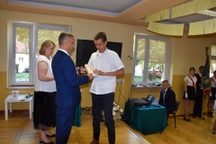 Dyrektor szkoły wręcza uczniowi nagrodę, w tle okno, telewizor