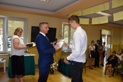 Dyrektor szkoły wręcza uczniowi nagrodę, w tle okno, telewizor