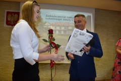 Dyrektor szkoły wręcza uczennicy książkę, zdjęcie budynku szkoły, godło