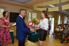 Dyrektor szkoły wręcza uczennicy książkę, zdjęcie budynku szkoły, godło