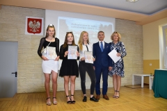 Dyrektor, nauczycielka i uczennice stoją z dyplomami w ręku