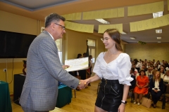 Wicestarosta Powiatu Piotrkowskiego wręcza uczennicy certyfikat ukończenia szkolenia, w tle telewizor, okno