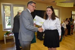 Wicestarosta Powiatu Piotrkowskiego wręcza uczennicy certyfikat ukończenia szkolenia, w tle telewizor, okno