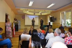 Na scenie stoi Wicestarosta Powiatu Piotrkowskiego i kierownik szkolenia praktycznego, nauczyciele siedzą, w tle zdjęcie budynku szkoły