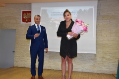 Dyrektor szkoły i kierownik internatu z kwiatami stoją, w tle godło, zdjęcie budynku szkoły