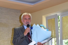 Kierownik szkolenia praktycznego stoi w jednej ręce trzyma mikrofon, w drugiej ręce trzyma kwiaty