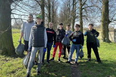 Uczniowie z workami wypełnionymi śmieciami stoją , w tle drzewa